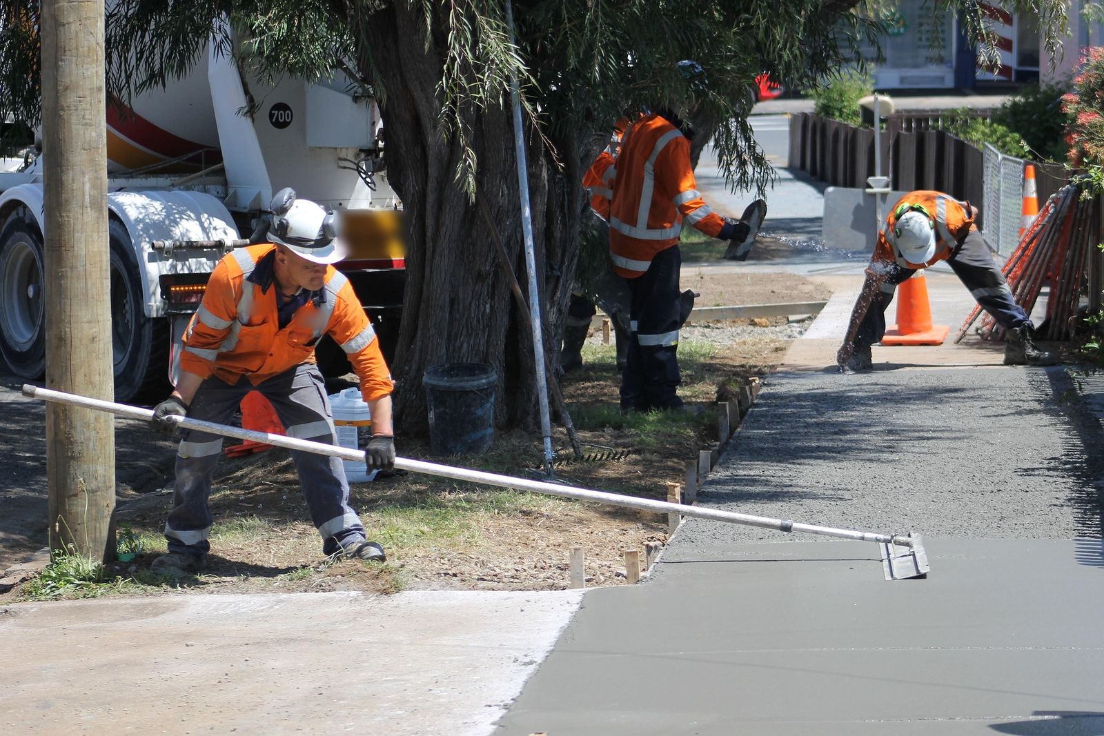 Una cuadrilla alisando una acera de concreto fresco junto a un camión mezclador