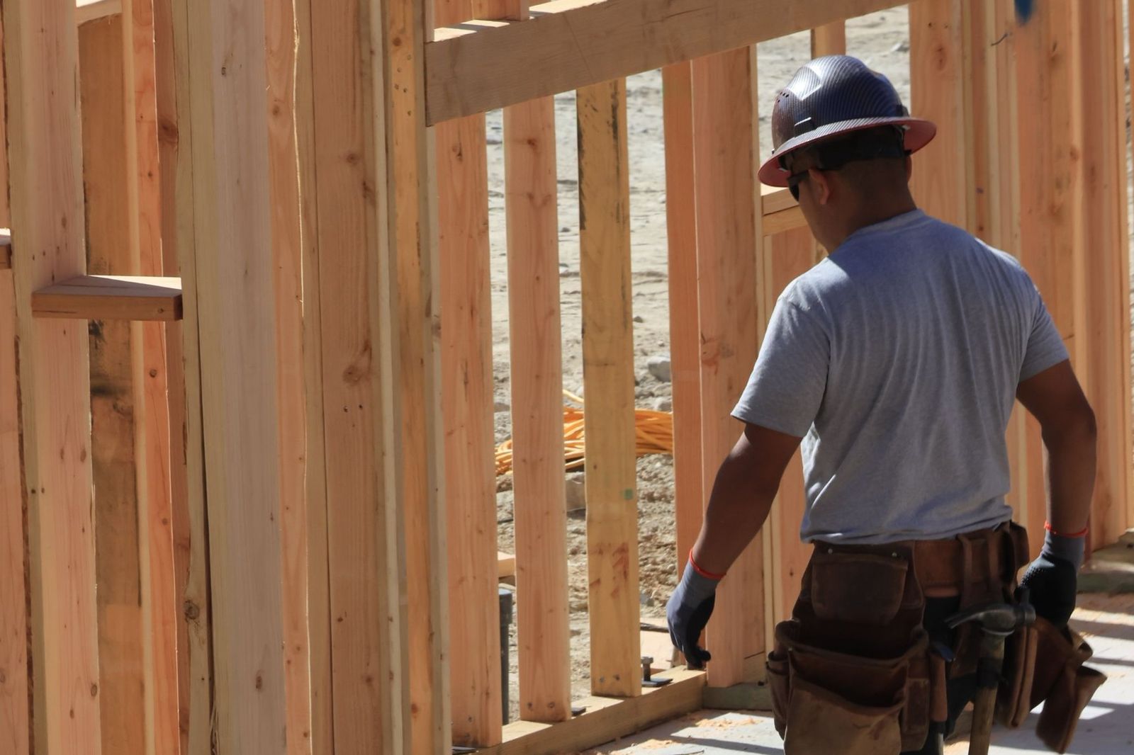 A framer with a hard hat and tool belt at a house under construction