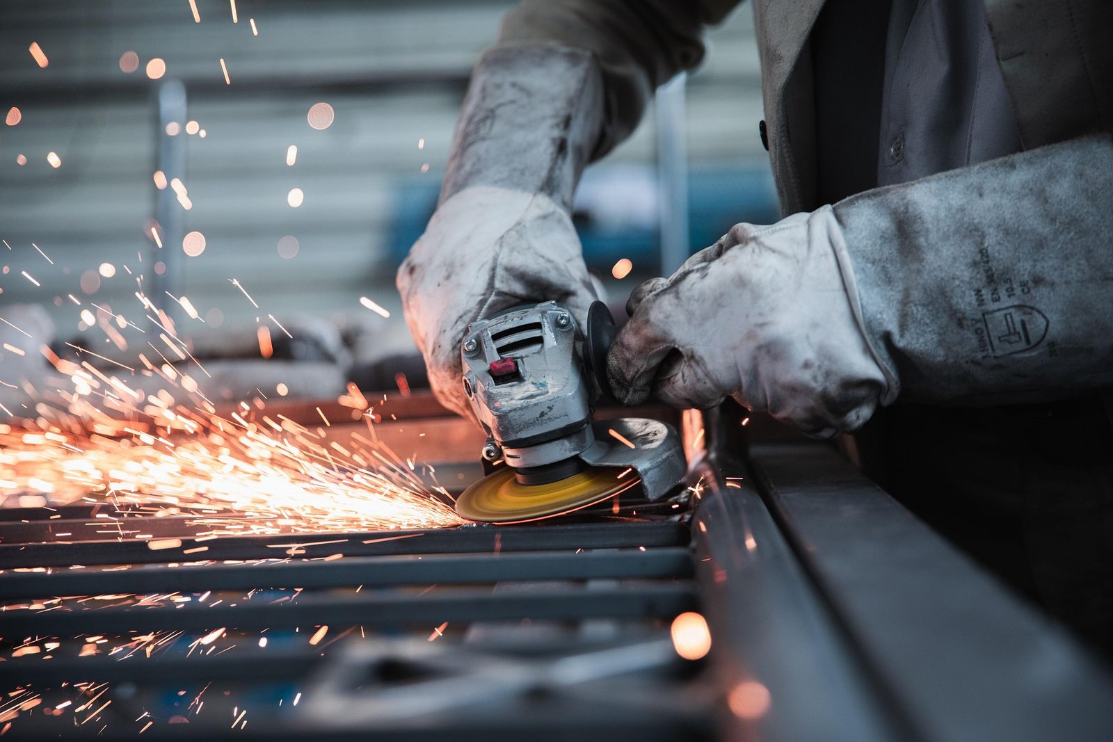 Un trabajador usando una esmeriladora en un taller de metal, con chispas