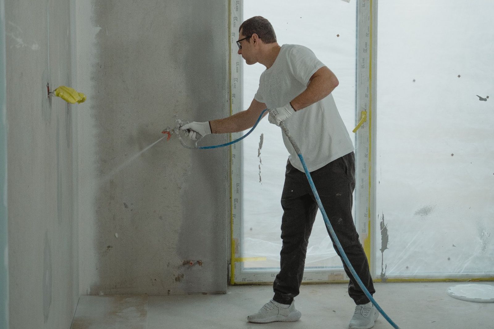 A painter using a paint sprayer on an interior wall