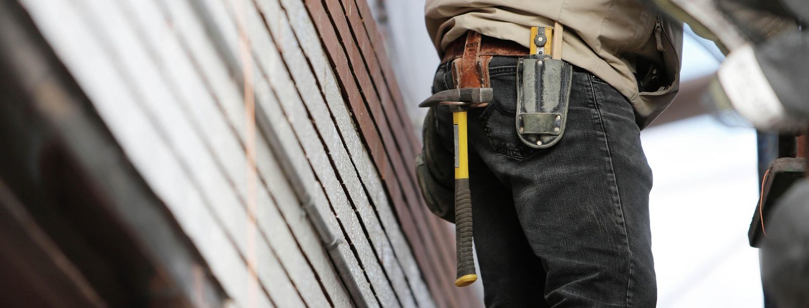 Un trabajador con un martillo en el cinturón de herramientas trabajando en un edificio de ladrillo